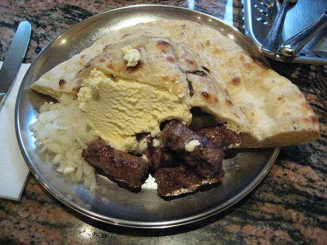 Cevapi may be served on a plate or in a flatbread, often with chopped onions, sour cream, kajmak, ajvar, cottage cheese, and other condiments.